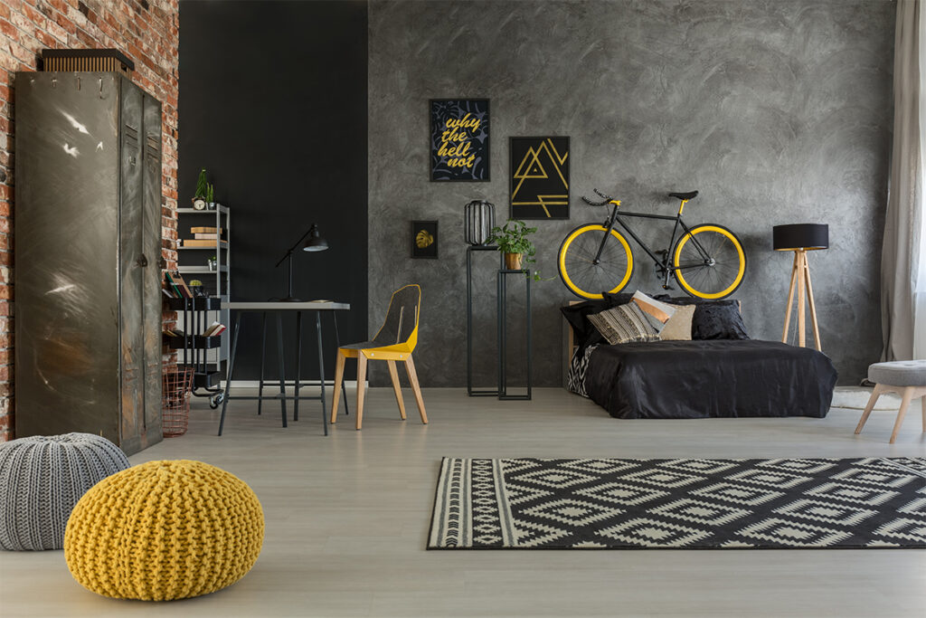 Rugmaker_Blog-Piece-SideImages_Grey apartment with bed, desk, chair, brick wall, yellow details