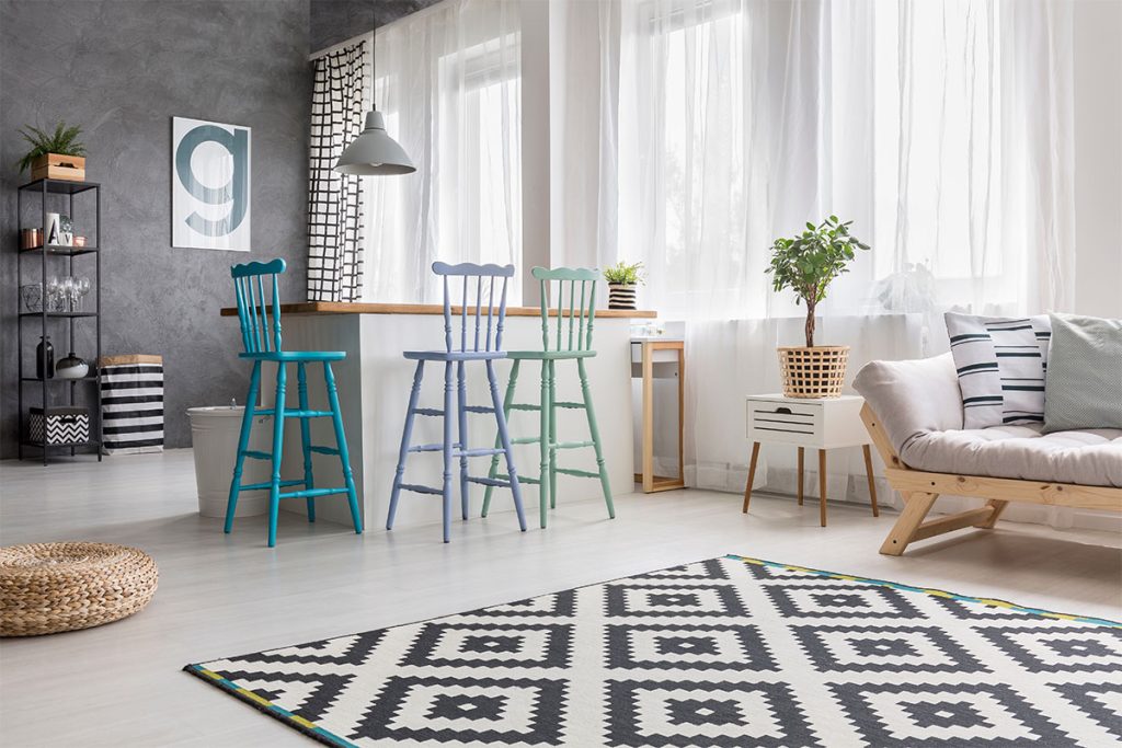 Rugmaker_Blog-Piece-SideImages_Geometric carpet in spacious living room with blue bar stools at kitchenette, pouf and ca