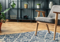 Rugmaker_Blog-Piece-Header_A grey chair standing on a patterned rug in front of black shelves and next to vases with pla