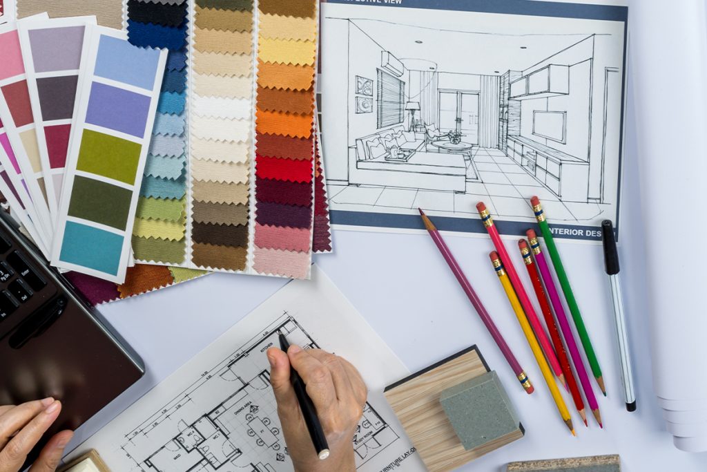 Rugmaker_Blog-Piece_Top view of architects hands drawing of modern house with material sample on creative desk