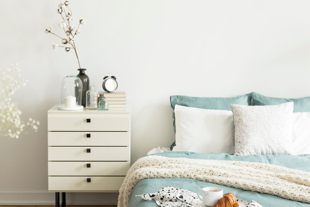 Rugmaker_Blog-Piece_A bright bedroom interior with sage green and white bedding, pillows on bed and a drawer nightstand