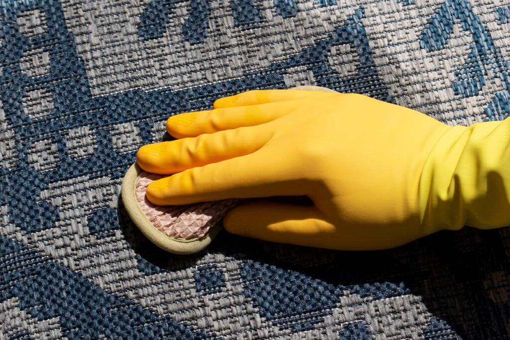 Rugmaker_Blog-Piece_Person cleaning an outdoor rug with soapy water weaqring rubber glove